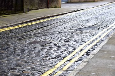 Dublin, İrlanda 'da ıslak bir kaldırımlı sokakta klasik tren rayları. Çift sarı çizgiler yan yana. 