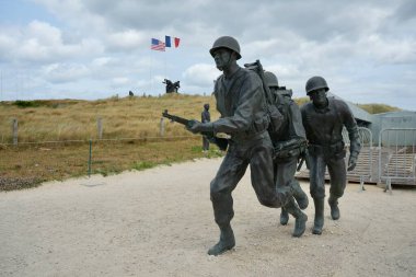Higgins Tekne Anıtı, bulutlu bir gökyüzünün altında arkasında Amerikan ve Fransız bayrakları olan bronz heykel. Utah Plajı, Fransa, 3 Temmuz 2023. 