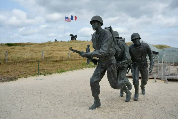 Higgins Tekne Anıtı, bulutlu bir gökyüzünün altında arkasında Amerikan ve Fransız bayrakları olan bronz heykel. Utah Plajı, Fransa, 3 Temmuz 2023. 