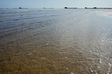 Dalgalar, Asnelles Sahili 'nde 2. Dünya Savaşı' ndan kalma dut limanı kalıntılarıyla sahilde tur atıyor. Arromanches, Fransa, 5 Temmuz 2023. 