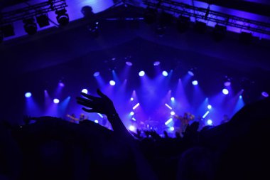 Siluet of Hands mavi sahne ışıklarıyla bir rock konserinde el sallıyor..