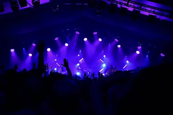 Silhouette of Hands waving at a rock concert with blue stage lighting.