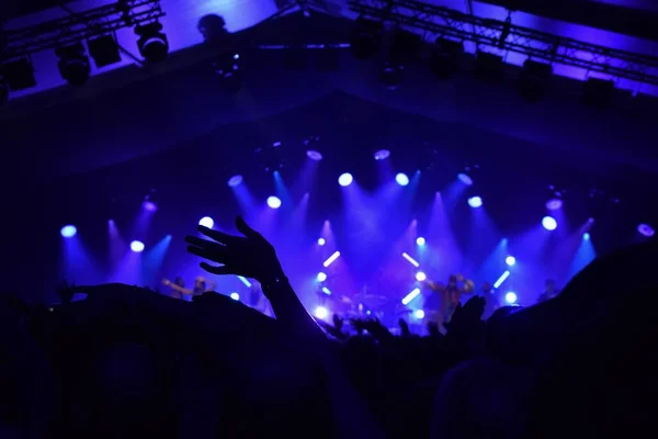 Silhouette of Hands waving at a rock concert with blue stage lighting.