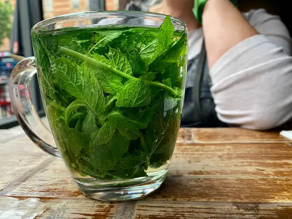 Clear cup of mint tea with freshly cut mint leaves, on a rustic wooden table.