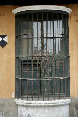 Turuncu duvarında demir parmaklıklar olan yeşil bir pencere. Lima, Peru. 