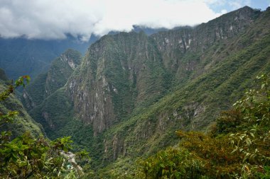 Machu Picchu, Peru 'da bulutlu bir gökyüzünün altında yeşilliklerle kaplı dağlar..