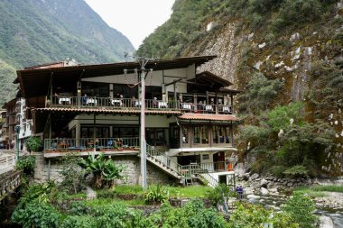 Aguas Calientes kasabasında Urubamba nehri ve arkasında dağlar olan binalar. Aguas Calientes, Peru, 6 Ekim 2023. 