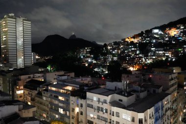 Gece bulutlu bir gökyüzünün altında İsa 'nın Heykeli' nin olduğu bir tepedeki binalar. Rio de Janeiro, Brezilya, 28 Ekim 2023. 