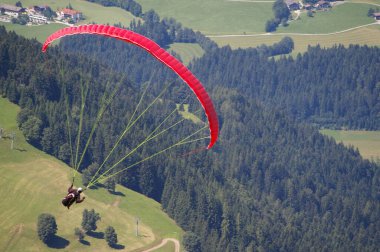 Aşağıdaki çayırların ve ormanların üzerinde uçan kırmızı bir paraglider. Hopfgarten im Brixental, Avusturya, 26 Temmuz 2009. 