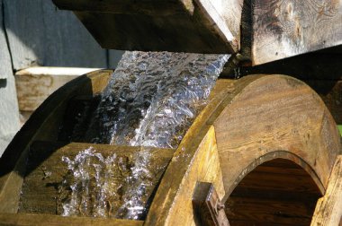 Taze, soğuk, berrak su, güneş ışığında ahşap bir su çarkının üzerinden akıyor.. 