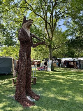 Ünlü hasır keman, Cambridge Halk Festivali 'nde tilki çalıyor. Ağaçların gölgesinde, arkada tezgahlar var. Cambridge, İngiltere, İngiltere. 27 Temmuz 2024. 