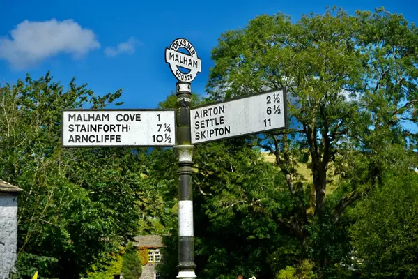 stock image Vintage Iron road sign under a blue sky with trees behind. Malham, Yorkshire Dales, England, UK. August 14, 2024. 