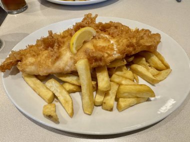 Geleneksel İngiliz Balık ve Patates kızartması. Bir dilim limonla birlikte beyaz bir tabakta haşlanmış morina balığı..