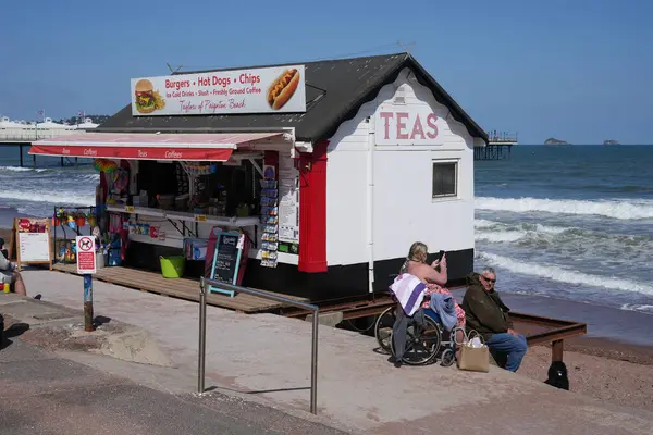 Paignton sahilindeki bir kafenin önünde oturan turistler. Paignton, Devon, İngiltere, İngiltere. Mayıs 2025. 