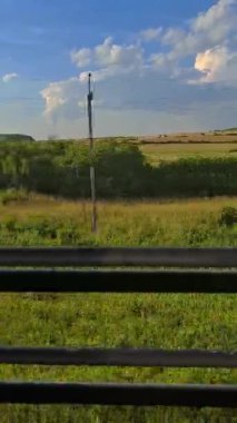 Trenin penceresinden kırsal alana bakın. Hareket halindeki trenin penceresinden yeşil alan ve mavi gökyüzü manzarası.