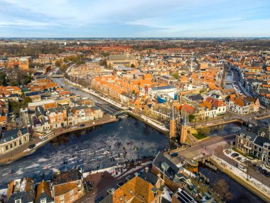 İnsanlar Sneek, Friesland 'daki tarihi Watergate' in önünde donmuş suda buz pateni yapıyorlar. Eski tarihi Sneek kasabasıyla birlikte insanlar kış boyunca donmuş suda buz pateni yapıyorlar.. 