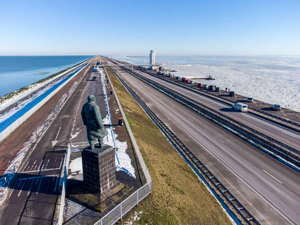在一个寒冷的冬日里 我们看到在瓦登海仍是液体的情况下 它完全冻僵了 这条公路沿着荷兰的一条长堤坝 蓝蓝的天空明亮 工程师莉莉的雕像傲然挺立 — 图库照片