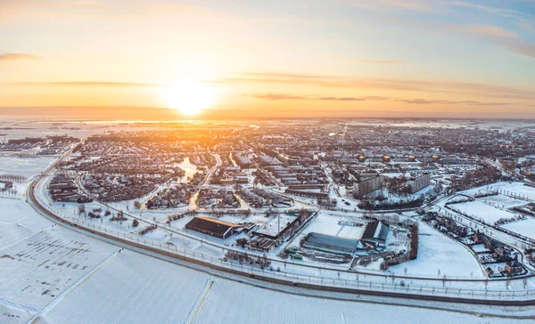 stock image The yellow, golden, rising sun illuminates a small city in winter conditions. The houses, meadows and streets are covered in white snow, the water is frozen.