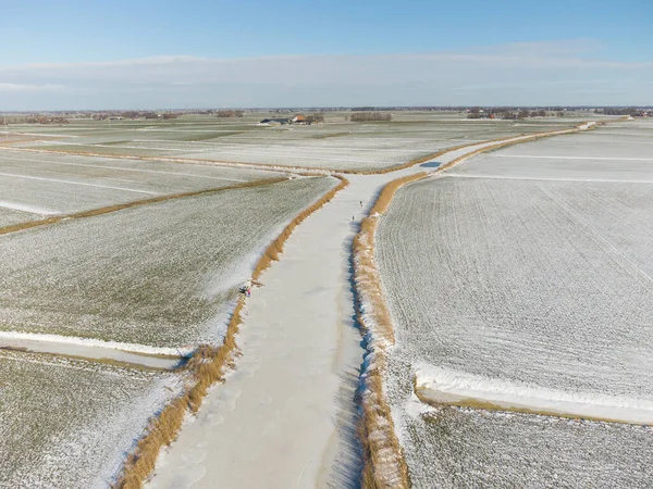 stock image A frozen river in Friesland, The Netherlands. under a blue sky and with golden reed flanking the water. Light frost and snow is visible on the pastures