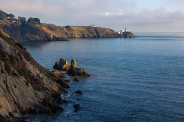 Howth Island, Dublin, İrlanda 'da yürüyüş parkurunda. Uzakta ikonik beyaz Baily Deniz Feneri var. Sakin denizin üzerinde mavi bir gökyüzünün altında sis vardır. Yüksek, dik uçurumlar. Sakin güneşli sisli bir sabah
