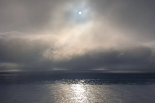 A fog bank lies offshore, the rolling clouds are low above the water. Foggy morning in calm sunny conditions The golden rays of the sun illuminate the scene. Soft light. Flat surface and glassy water