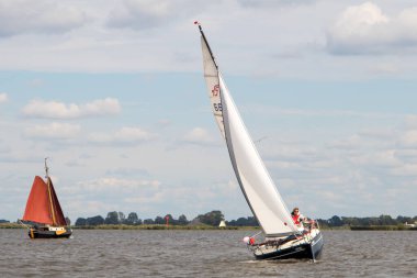 Hollanda 'daki bir gölde tipik bir Hollanda bulutlu gökyüzü altında kanat çırpan bir yelkenlinin drone çekimi. Yüksek kalite fotoğraf