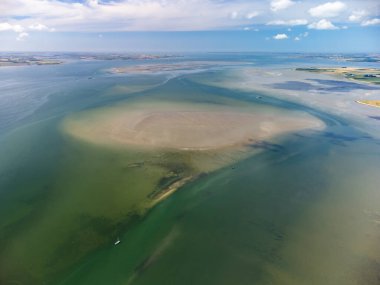 Drone shot of a sailboat with dinghy anchored under typical Dutch blue sky on a lake in Zeeland, The Netherlands. A shallow sandbank is close by, currents are visible.High quality photo