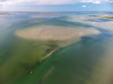 Drone shot of a sailboat with dinghy anchored under typical Dutch blue sky on a lake in Zeeland, The Netherlands. A shallow sandbank is close by, currents are visible.High quality photo