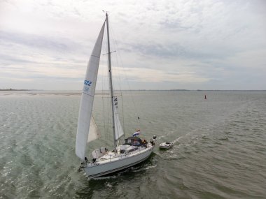 Drone shot of sailboats under typical Dutch cloudy sky on a lake in The Netherlands. Small bow waves and passing a sandbank on the Oosterschelde, The Netherlands. High quality photo