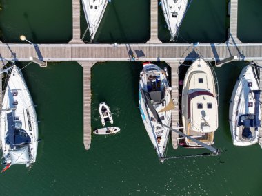 A top-down view of a marina in Zeeland, The Netherlands. A few sailing boats, a SUP and a dinghy moored at the jetty. High quality photo