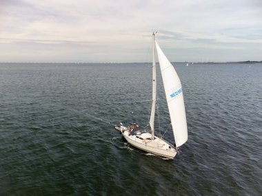 Drone shot of sailboats under typical Dutch cloudy sky on a lake in The Netherlands. Small bow waves and passing a sandbank on the Oosterschelde, The Netherlands. High quality photo