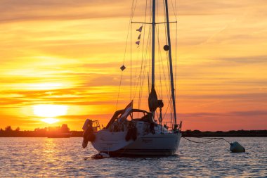 Sailing boat anchored on a mooring with dramatic sunset. Orange skies with cirrus clouds.Taken in Zeeland, The Netherlands. High quality photo