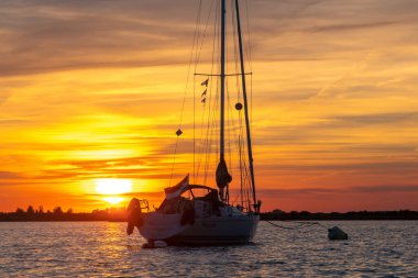 Sailing boat anchored on a mooring with dramatic sunset. Orange skies with cirrus clouds.Taken in Zeeland, The Netherlands. High quality photo