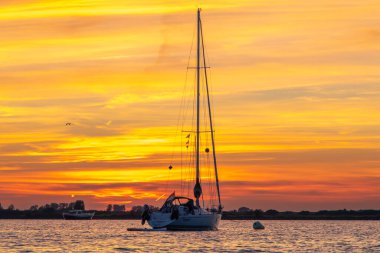 Sailing boat anchored on a mooring with dramatic sunset. Orange skies with cirrus clouds.Taken in Zeeland, The Netherlands. High quality photo