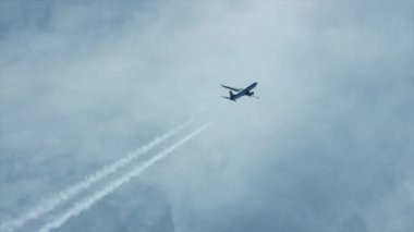 Airplane seen in silhouette with contrails seen from above with clouds. White water condensation trail behind aircraft and layered colourful clouds. High quality FullHD footage