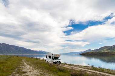 A single campervan parked near Lake Hawea, New Zealand. A small fence leads into the frame from the left. Bright blue sky with Cirrus clouds. High quality photo