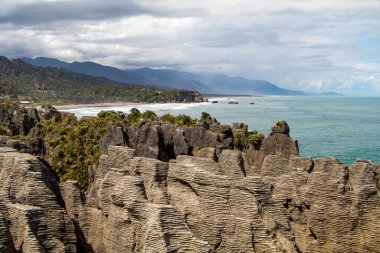 Close view of the Pancake Rocks near Punakaiki, New Zealand. Ocean and hills in the background. Structured, moody clouds. High quality photo
