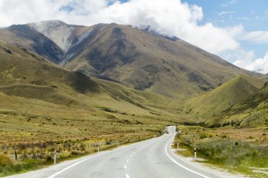 Winding and scenic road in New Zealand, with tall mountains and a blue sky. High quality photo