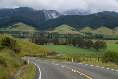 Winding and scenic road in New Zealand, with tall mountains and green grasslands. Cloudy sky. High quality photo