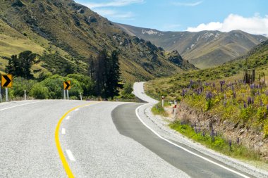 Winding and scenic road in New Zealand, with tall mountains and a blue sky. High quality photo