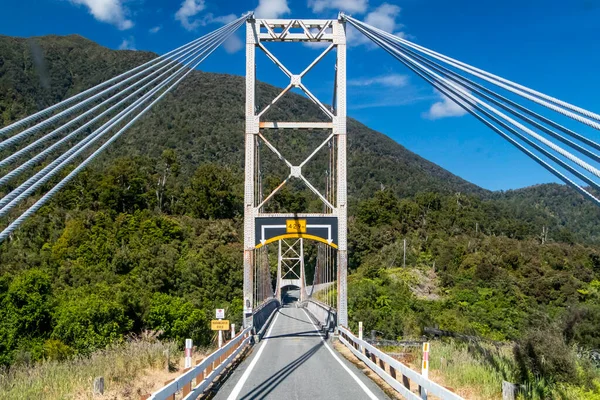 Narrow road over a suspension bridge in New Zealand. Single track road. Green hills and a bright blue sky. Driver perspective. High quality photo