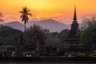 Tayland 'daki Sukhothai Tarihi Parkı' ndaki antik tapınaklar. Tarihi kırmızı tuğla yapılar ve tapınaklar. Siluet turuncu günbatımı gökyüzüne karşı. Palmtree. İnsan yok. Yüksek kalite fotoğraf