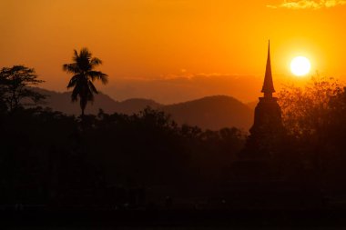 Tayland 'daki Sukhothai Tarihi Parkı' ndaki antik tapınaklar. Tarihi kırmızı tuğla yapılar ve tapınaklar. Siluet turuncu günbatımı gökyüzüne karşı. Palmtree. İnsan yok. Yüksek kalite fotoğraf
