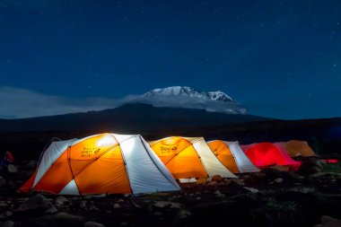 Kilimanjaro Dağı 'ndan önce gece boyunca turuncu çadırlar içeriden aydınlatıldı. Yıldızlar ve Samanyolu görünür. Yüksek kalite fotoğraf