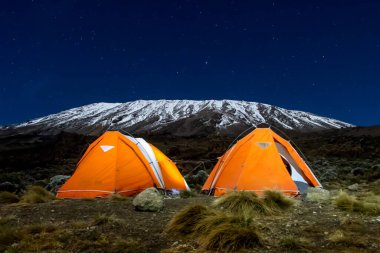 Kilimanjaro Dağı 'ndan önce gece boyunca turuncu çadırlar içeriden aydınlatıldı. Yıldızlar ve Samanyolu görünür. Yüksek kalite fotoğraf