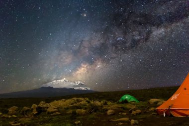 Kilimanjaro Dağı 'ndan önce gece boyunca turuncu çadırlar içeriden aydınlatıldı. Yıldızlar ve Samanyolu görünür. Yüksek kalite fotoğraf