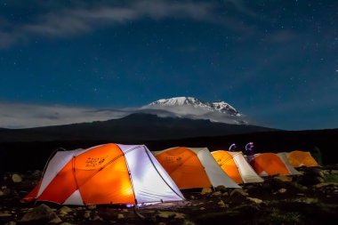 Kilimanjaro Dağı 'ndan önce gece boyunca turuncu çadırlar içeriden aydınlatıldı. Yıldızlar ve Samanyolu görünür. Yüksek kalite fotoğraf