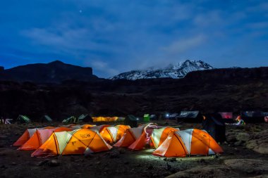 Kilimanjaro Dağı 'ndan önce gece boyunca turuncu çadırlar içeriden aydınlatıldı. Yıldızlar ve Samanyolu görünür. Yüksek kalite fotoğraf
