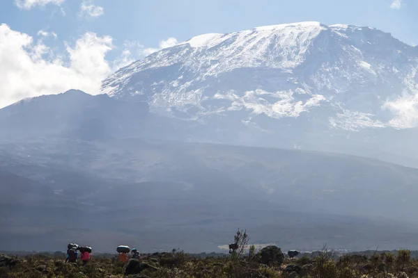 Mount Kilimanjaro with native porters carrying pack on their heads. Hiking trail to the top. Mountain top covered in Snow. High quality photo