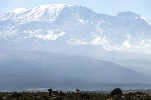 キリマンジャロ山では 地元のポーターが頭にパックを運んでいます 上へのハイキングコース 山頂は雪に覆われている 高品質の写真 — ストック写真